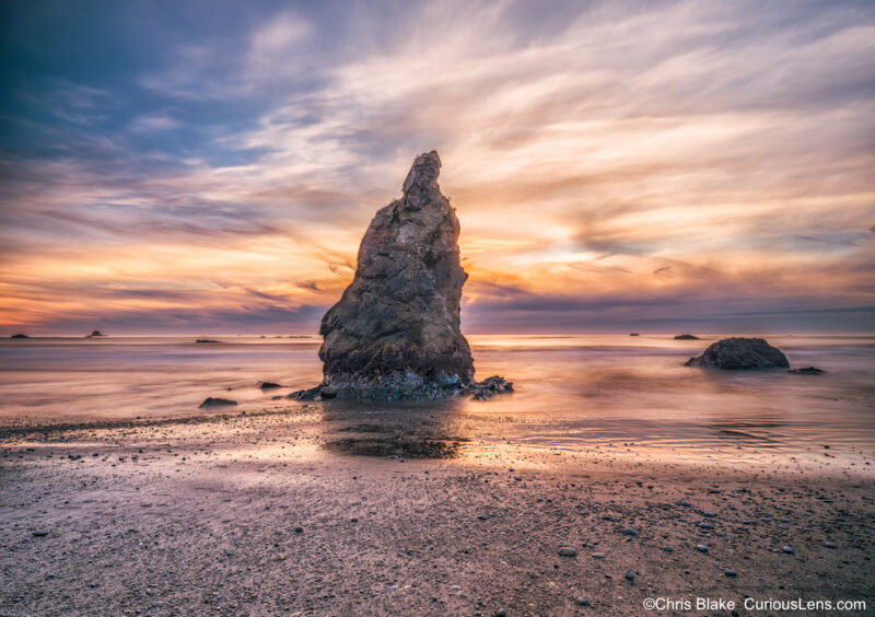 Sunset at Kalaloch and Ruby Beaches, Olympic Peninsula with sea stack, colorful clouds, soft blurred waves, and warm light glowing behind the rock.