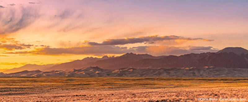 Sunset at Great Sand Dunes with Sangre de Cristo Mountains, yellow evening light, breaking clouds, and dramatic landscape.