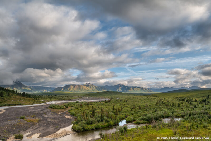 Savage River canyon with unique Yukon-Tanana Terrane geology, river meandering through sediment bed towards distant mountains, and ethereal light from breaking clouds.