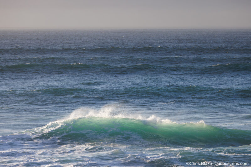 Massive wave breaking near Thor’s Well in Cooks Chasm, Oregon coast, during a king tide at sunset with stormy skies and illuminated sea spray.