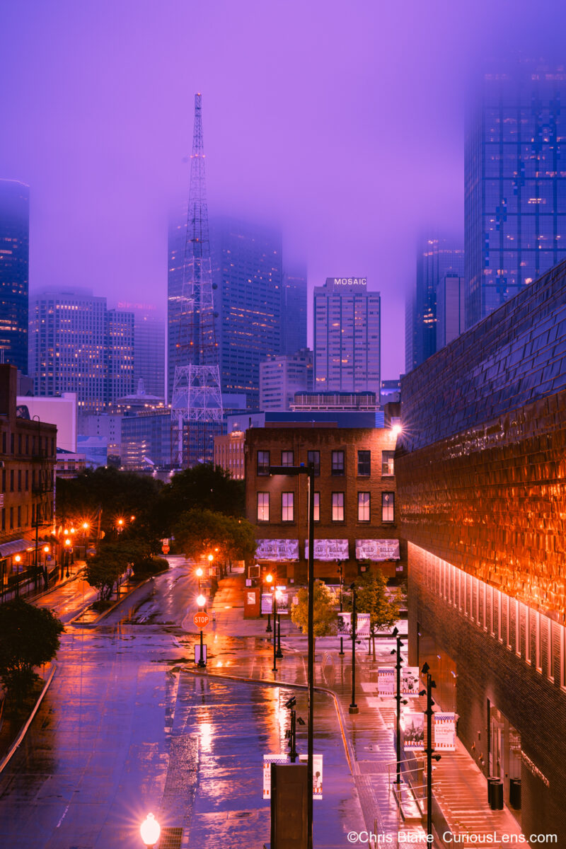 Dallas skyline at sunrise with storm clouds, city lights, and blue and purple colors.