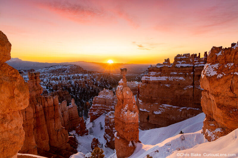 Winter morning at Bryce Canyon with Thor's Hammer hoodoo, glowing sun, dramatic clouds, and crimson-colored rock formations.