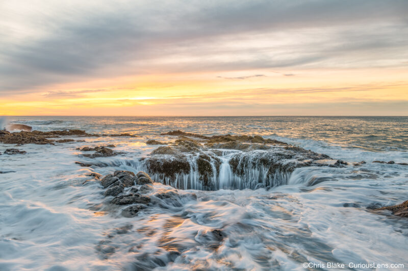 hor’s Well near Cape Perpetua, Oregon coast, at sunset with high tide, vibrant colors, and waves crashing around the collapsed sea cave.