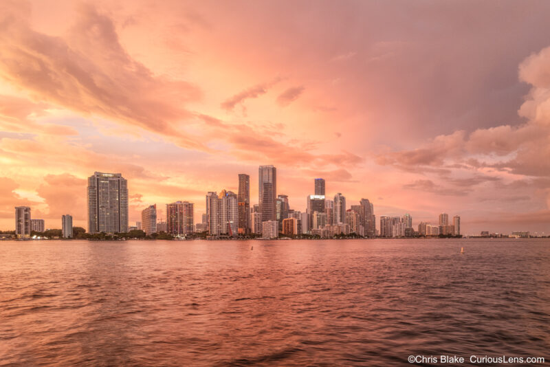 Miami skyline at sunset after summer storm with crimson sky, iconic buildings, and bay bathed in warm light.