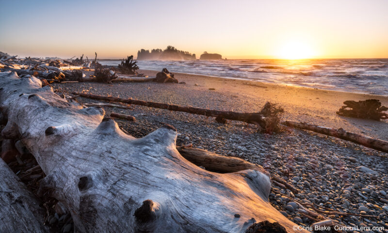 Rialto Beach at sunset with rocky beach, giant drift logs, seastacks, warm light, and glowing mist in late November.