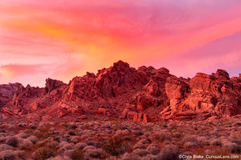 Valley of Fire State Park at sunset with red sandstone mountains, light clouds, red glow on desert floor, and winter scenery.