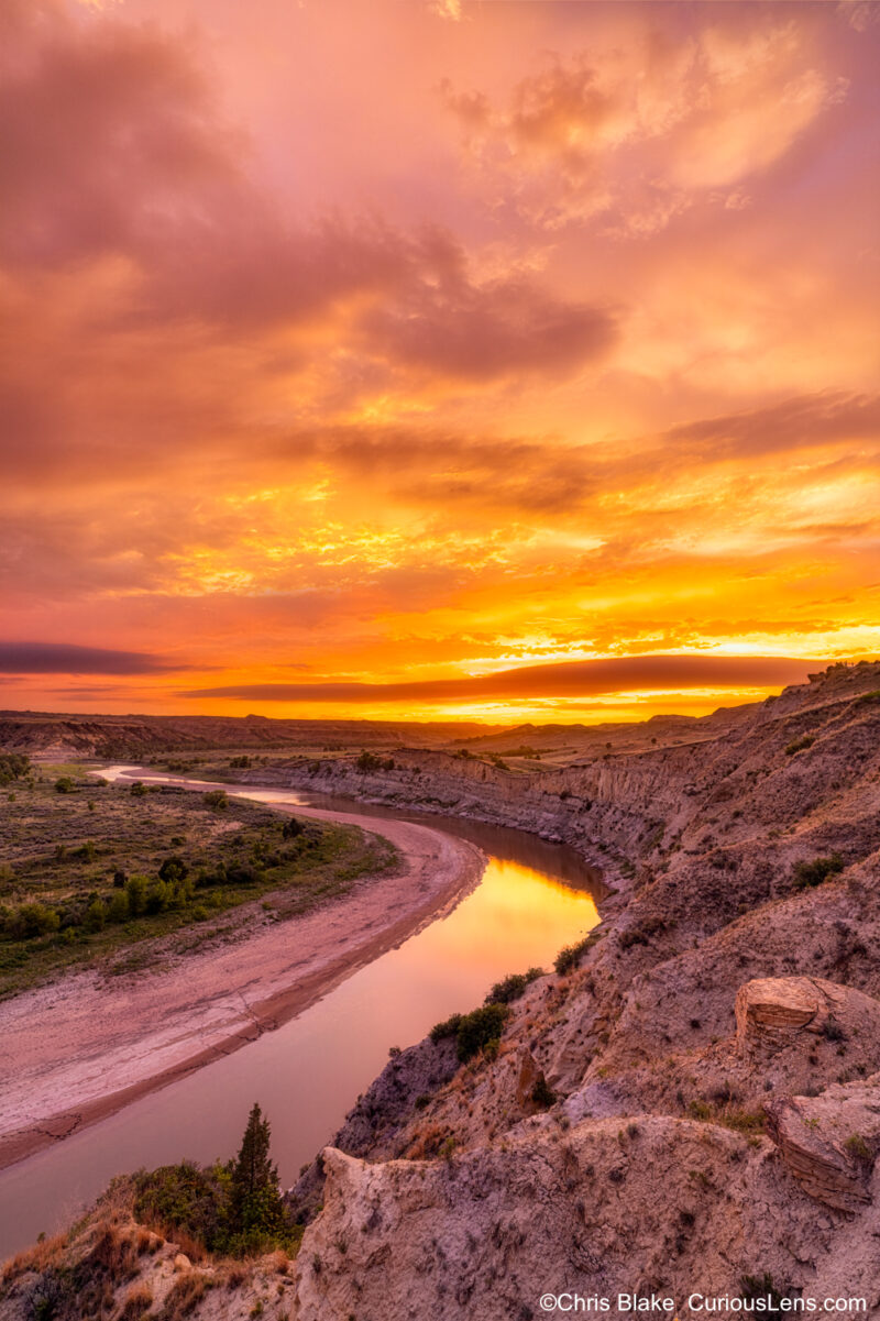 Wind Canyon at Theodore Roosevelt National Park with sunset lighting, soft yellow light, Little Missouri River reflecting retreating storm clouds.