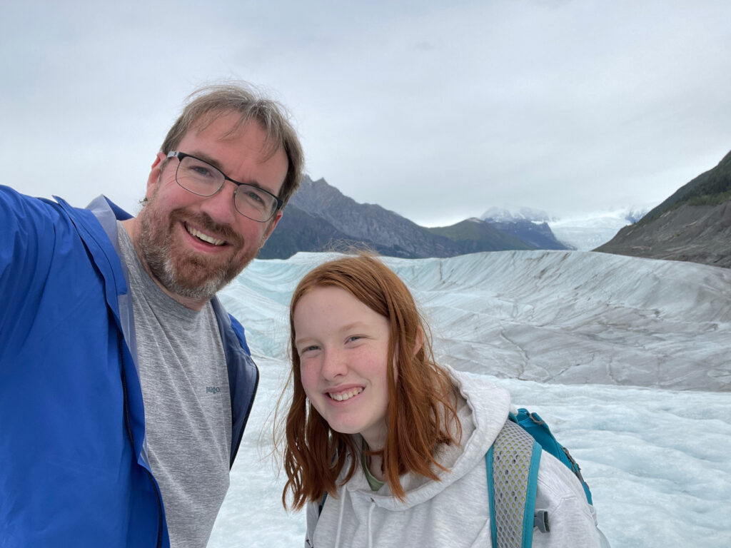 Cameron and myself pose for a photo on the Root Glacier - standing on the ice with mountains in the background. Both of us smiles and looking tired from the hike.