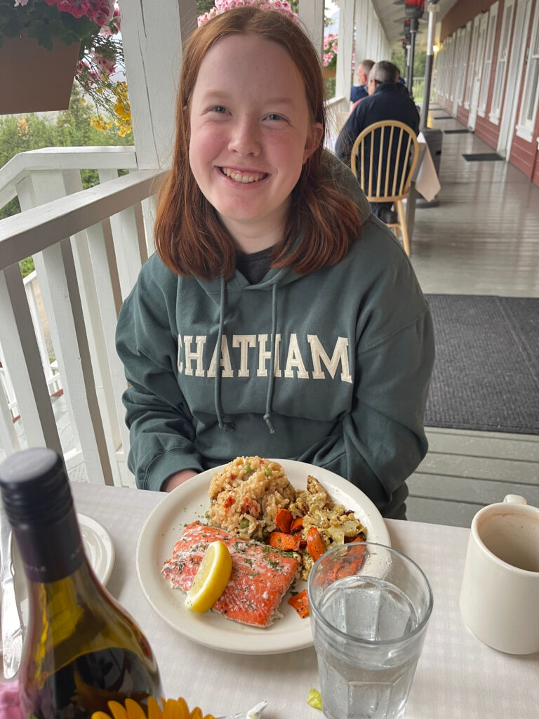 Cameron sitting at an outdoor table, on the deck at the Kennicott Glacier Lodge with a masive plate of food in front of her. 