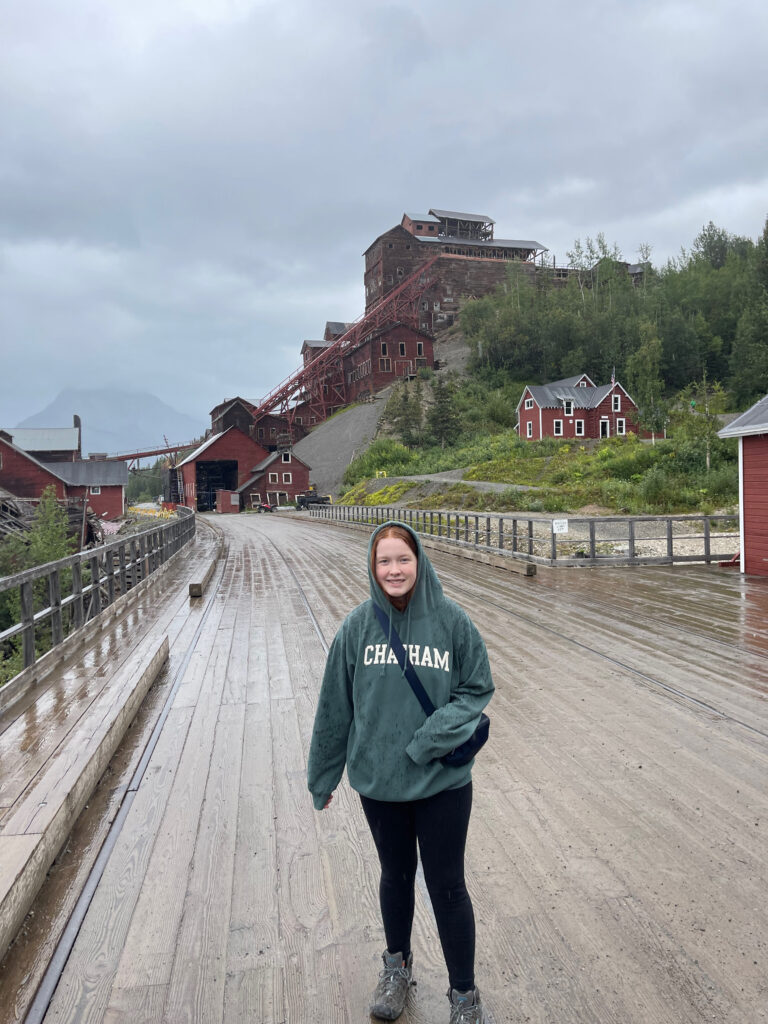 Cameron standing on the old wooden bridge that leads over the river to the Mill Building in Kennicott the massive wooden mill building can be seen in the background. 