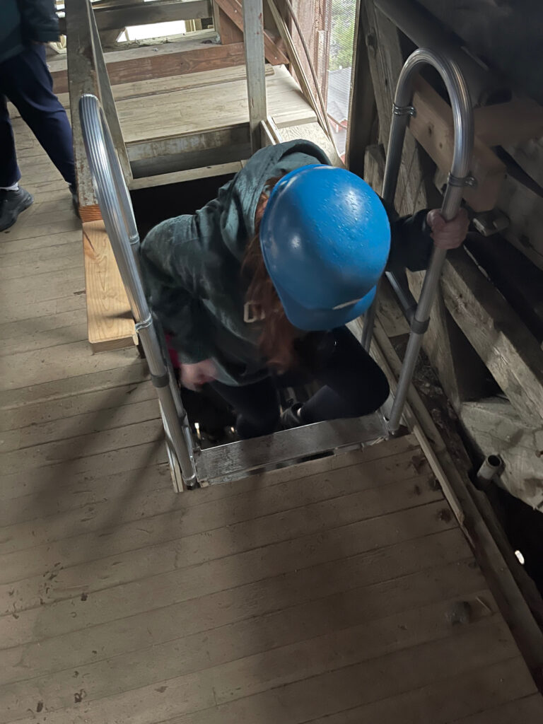 Cameron wearing a hard hat is climbing down a ladder inside the Mill in Kennicott.