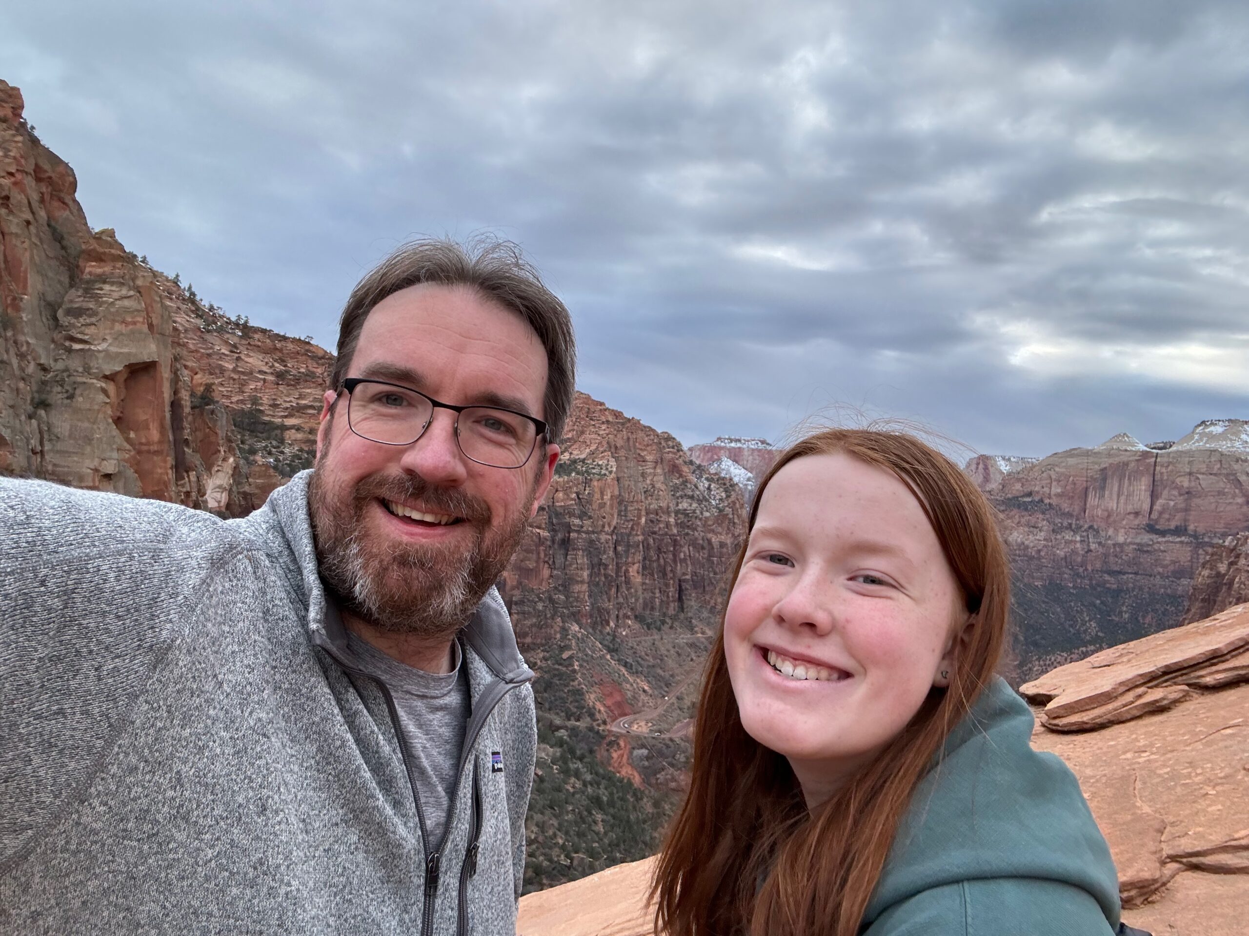 Cameron and myself pose for a photo at the end of the Canyon Overlook Trail in Zion National Park. Gray clouds and rain can be seen behind us along with the valley of Zion.