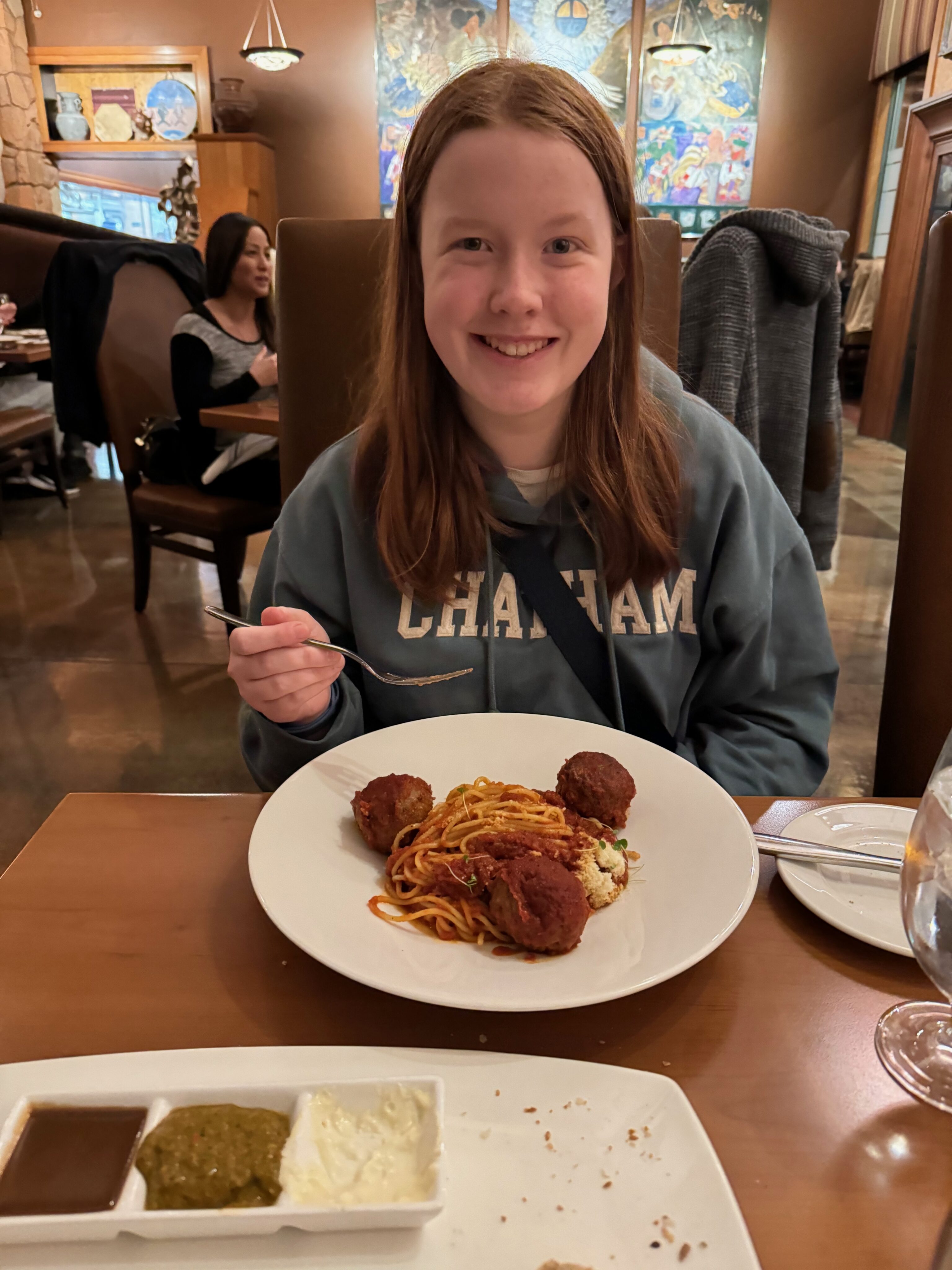 Cameron sitting at dinner at a fancy steakhouse in Springdale UT with a bowl of pasta in front of her and holding a fork.