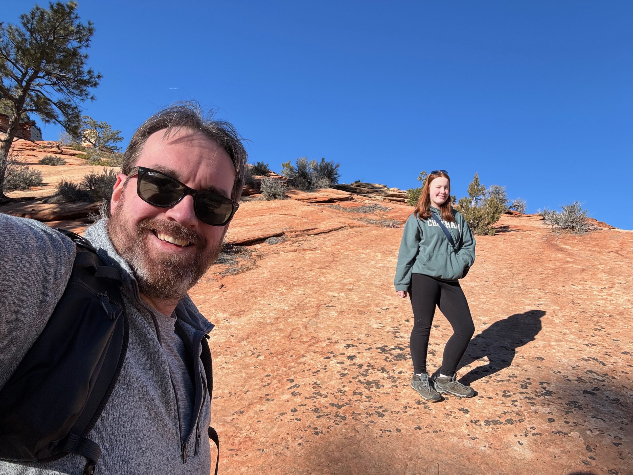 Cameron and myself stop half way up a sandstone mountain we are hiking on the east side of Zion for a picture. Me wearing sunglasses and ad Patagonia jacket. 