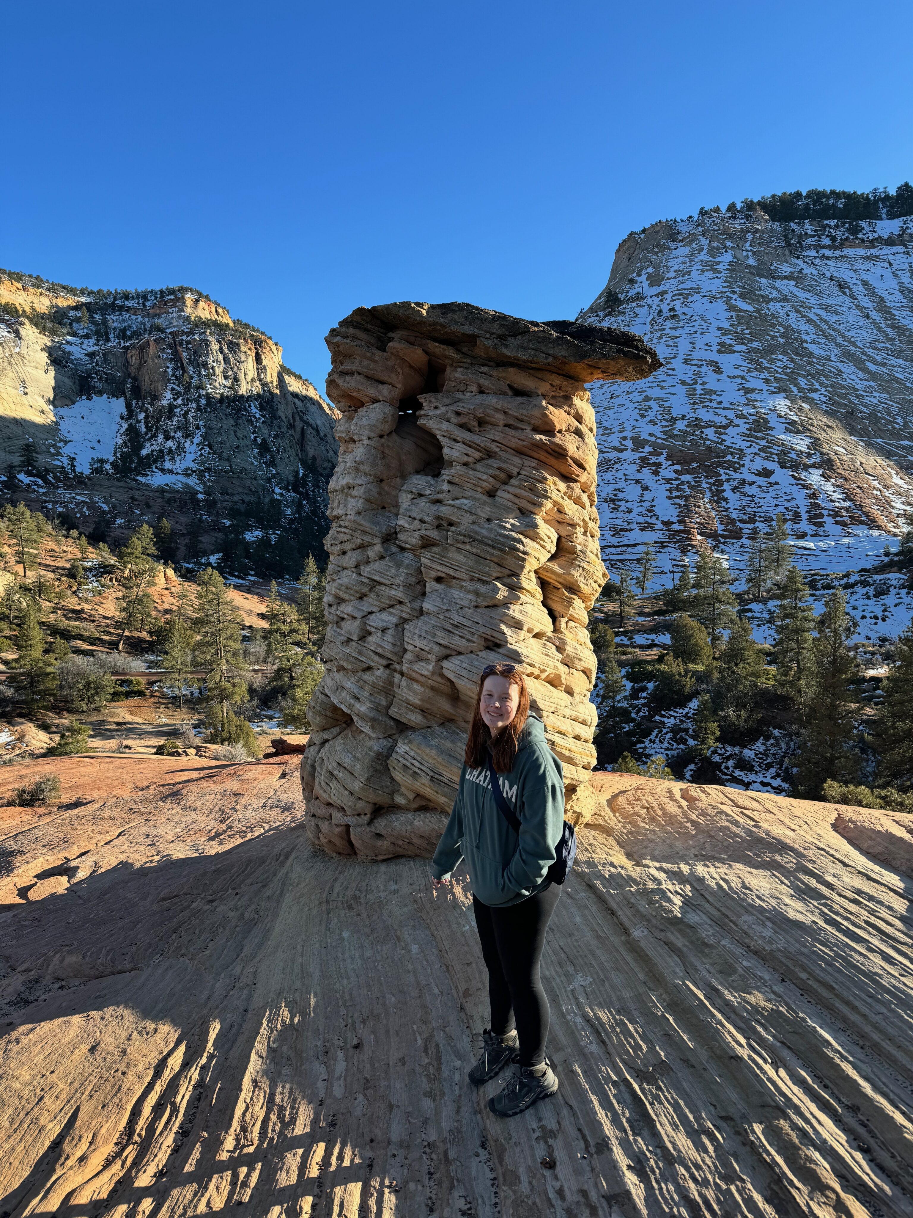 Cameron stands next to a massive rock formation, in the back country of Zion in the late afternoon light.