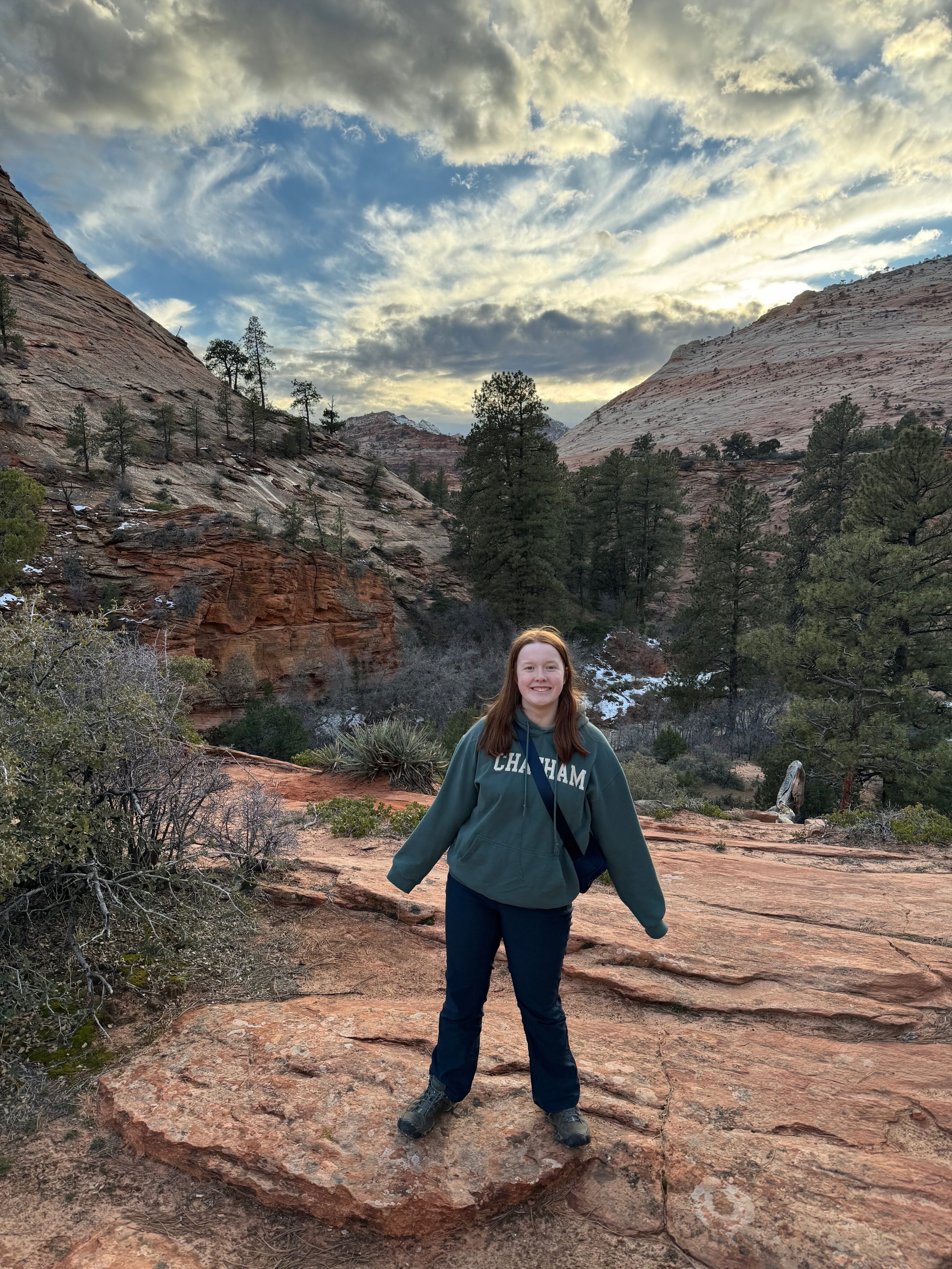 Cameron standing, smiling and poses for a photo at sunset in the east side of Zion. Amazing clouds and light can be see over the valley in the background.