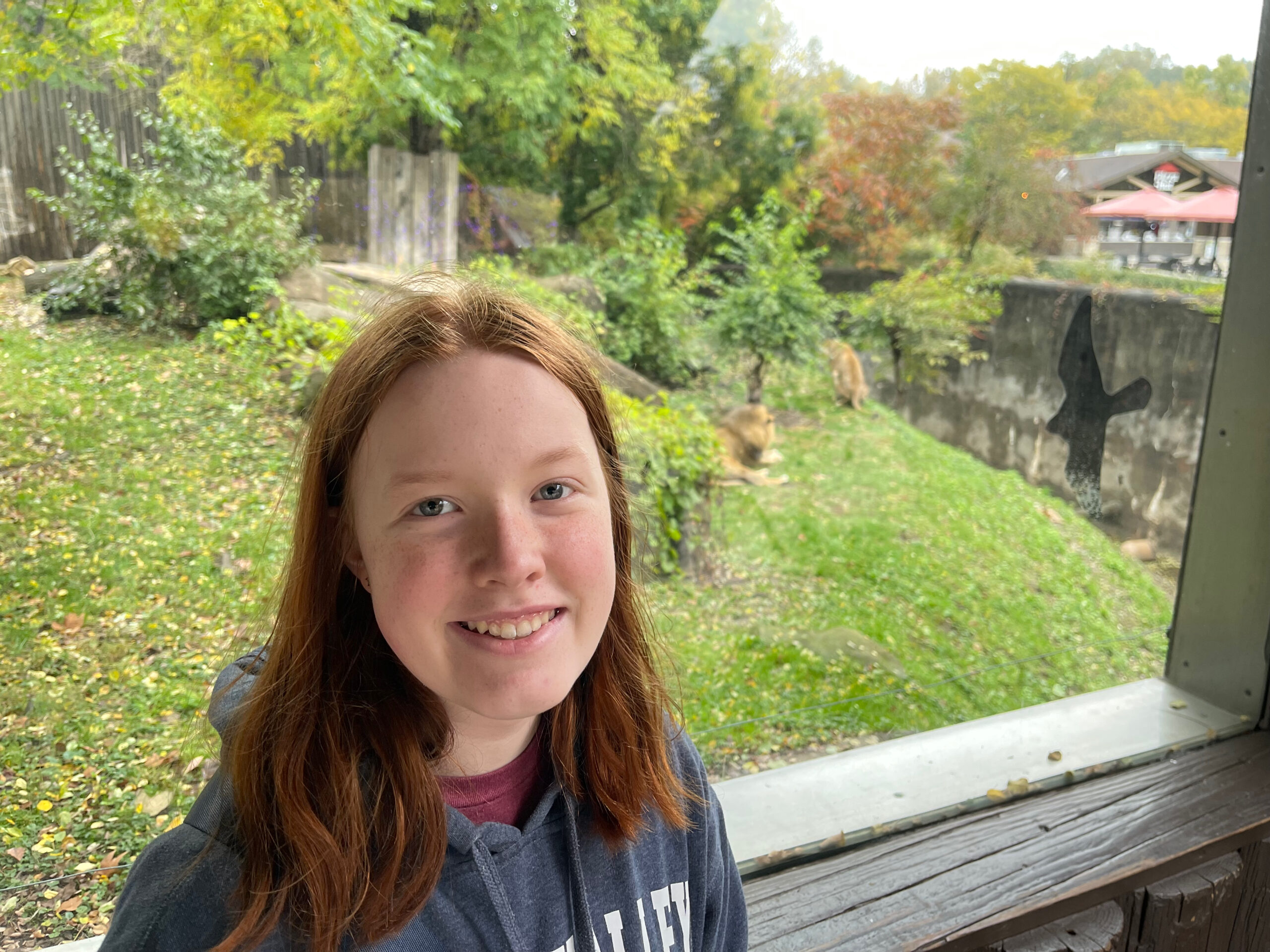 Cameron smiles at the zoo with a handful of resting lions behind her at MetroParks Zoo, Cleveland OH.