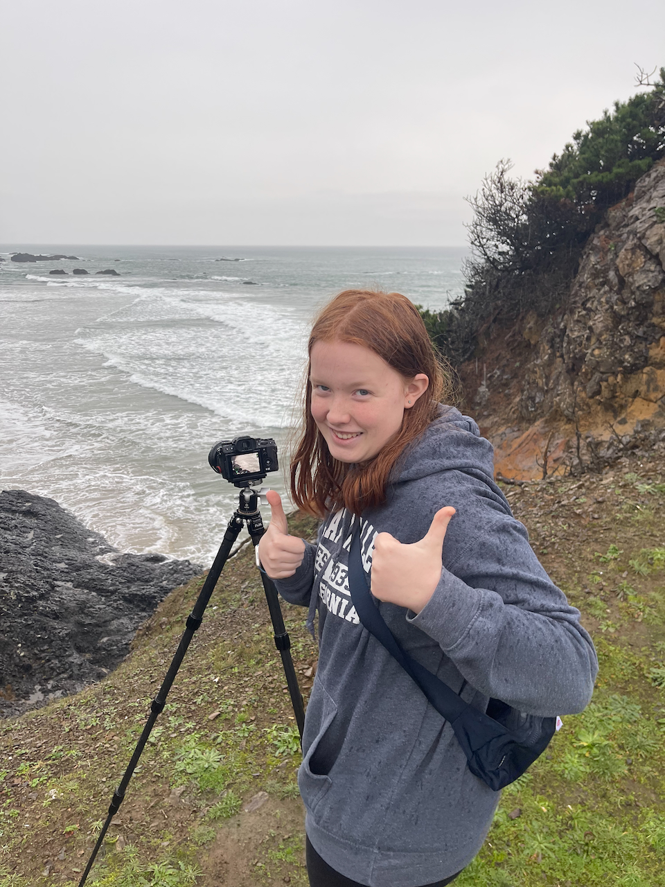 Cameron with her camera and tripod giving two thumbs up ontop of the dunes near Seal Rock on the Oregon coast. 