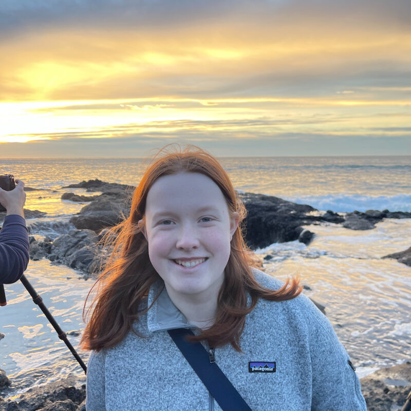 Cameron with a big smile, her red hair glowing for the yellow stunning sunset taking place behind her. You can also see part of my cameras tripod setup to capture Thors Well and the amazing sunset.