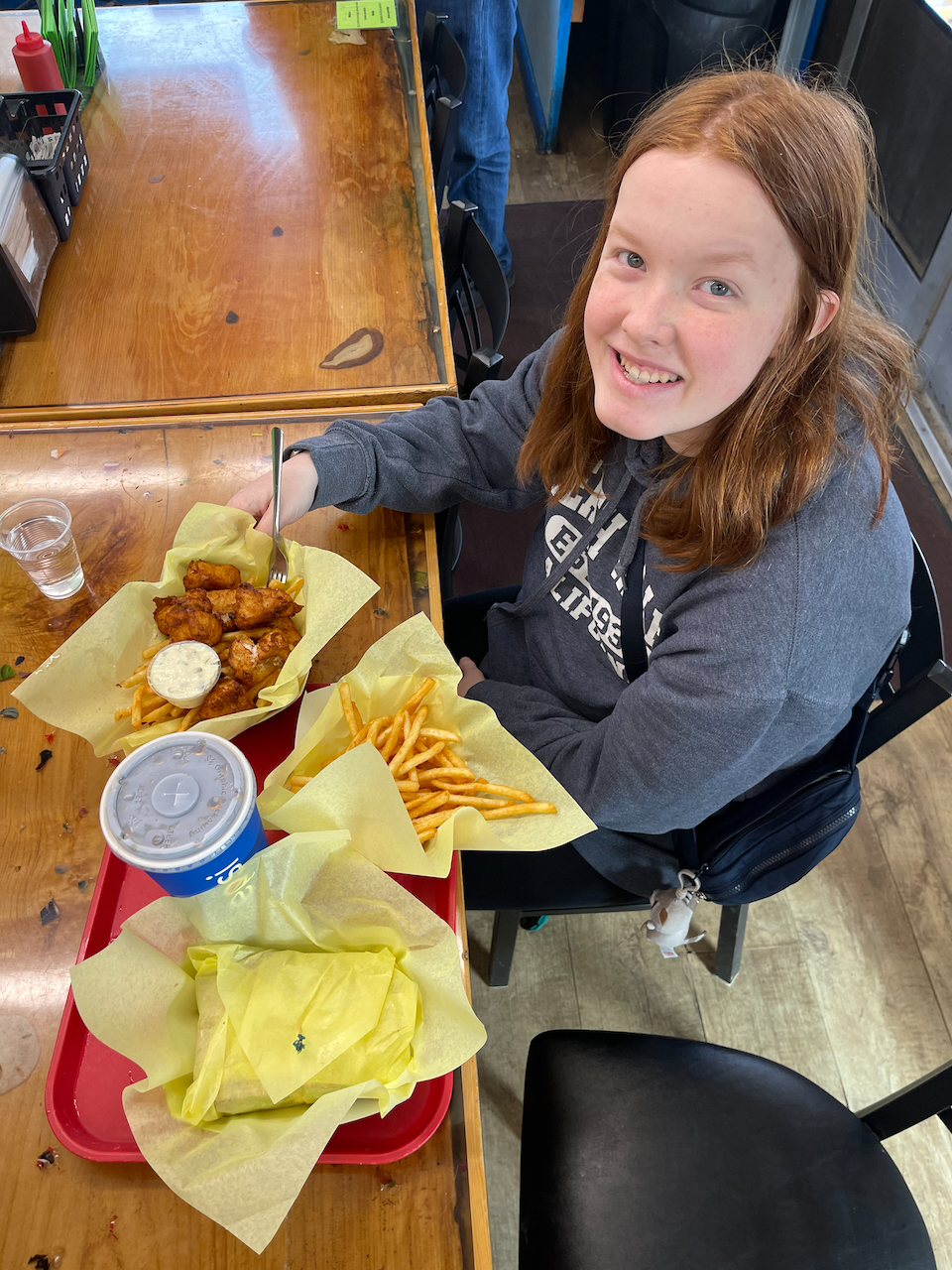 Cameron sitting at a table and looking up at the South Beach Fish Market with a table full of fresh fried fish in front of her.