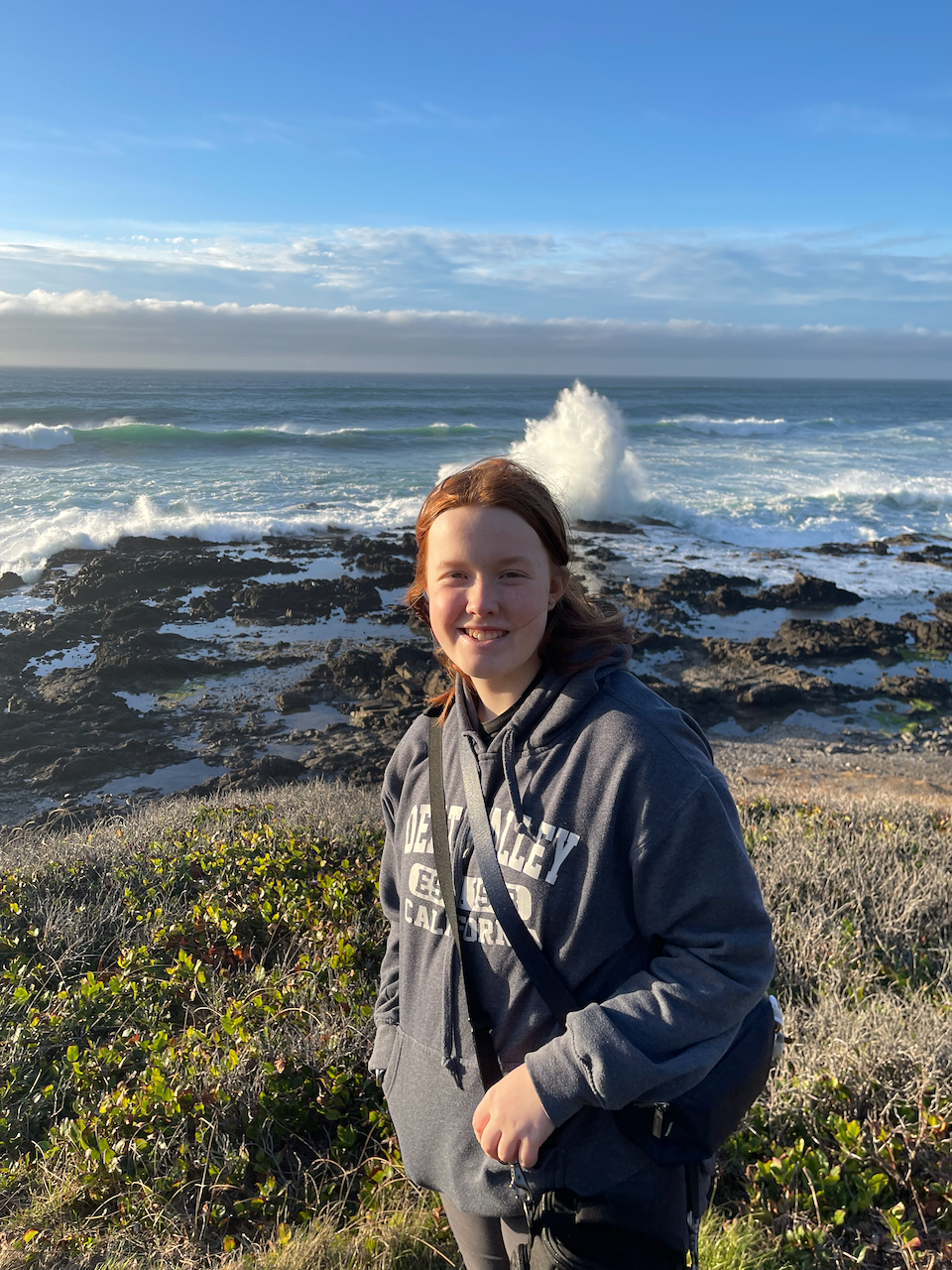 Cameron standing in the bluffs in the late afternoon light at Thors Well - as water explodes up from the massive waves.