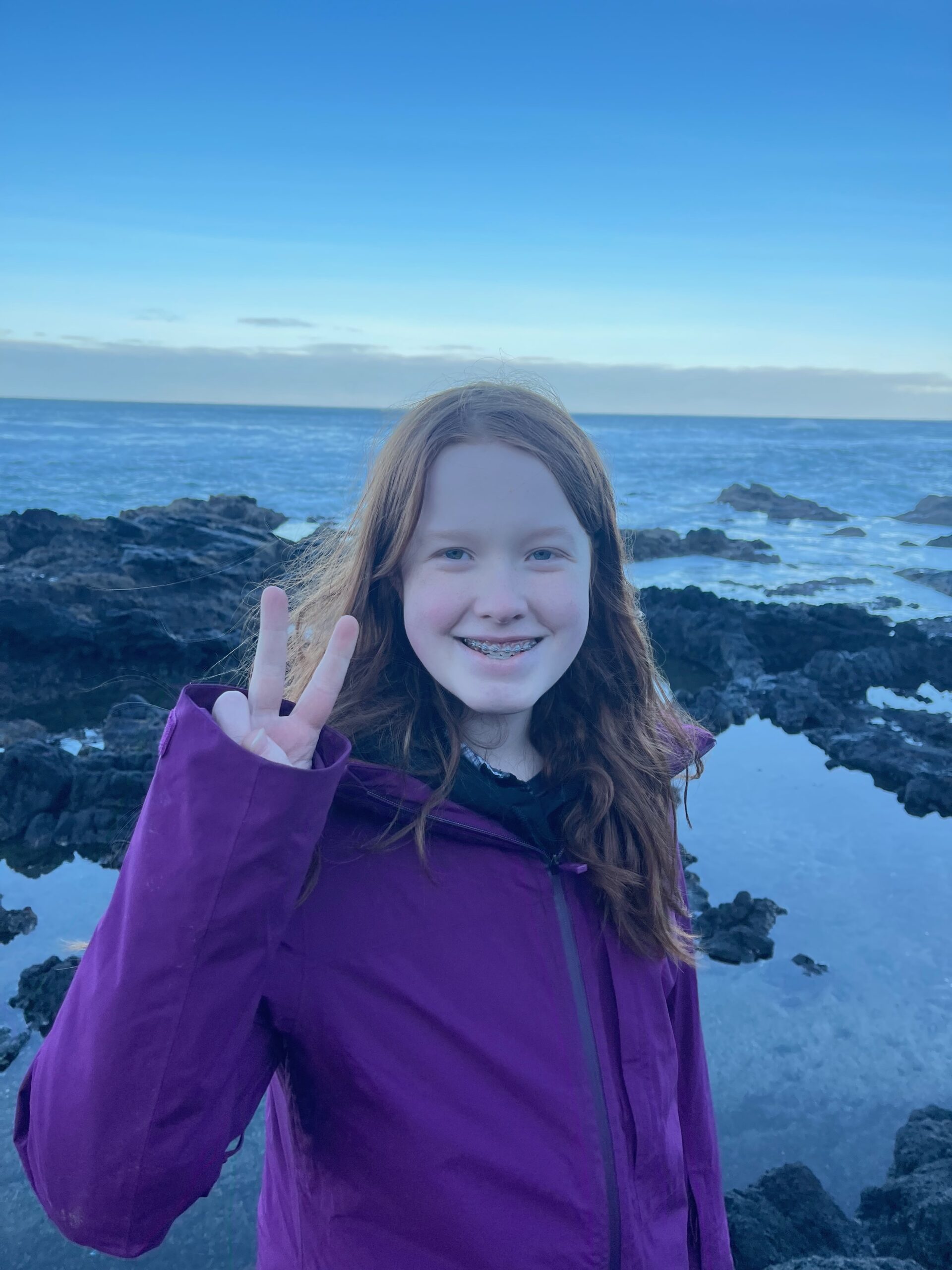 Cameron wearing a purple jacket, standing on the rocks at low tide at Thors Well.