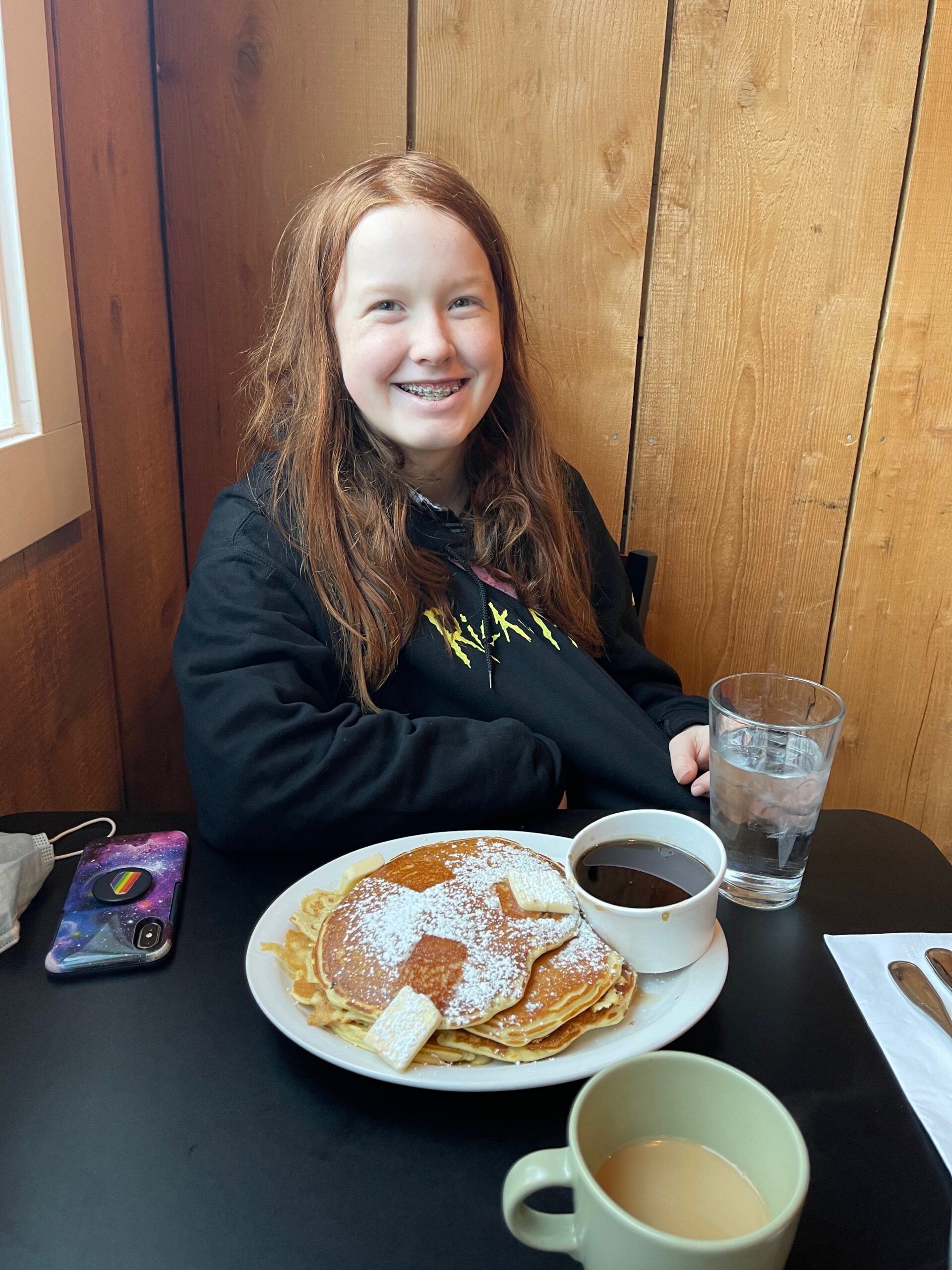 Cameron sitting at a breakfast table with a table full of pancakes in front of her with a massive smile on her face.