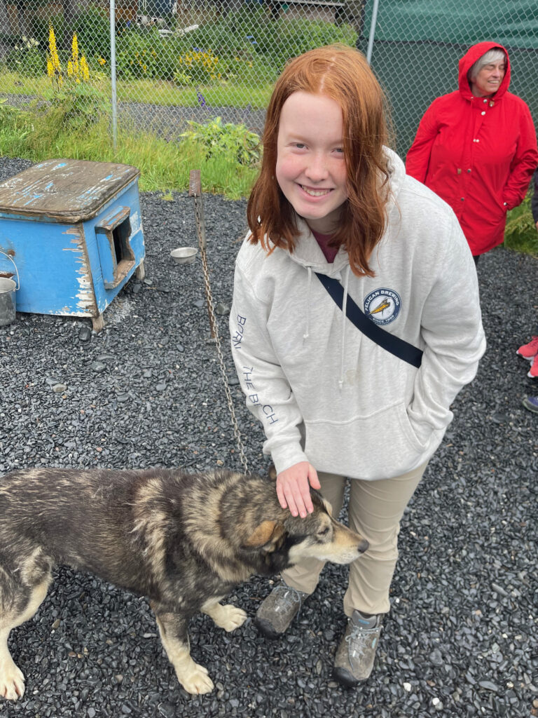 Cameron leans down to pet one of the sled dogs next to his kennel outside of Seward Alaska.