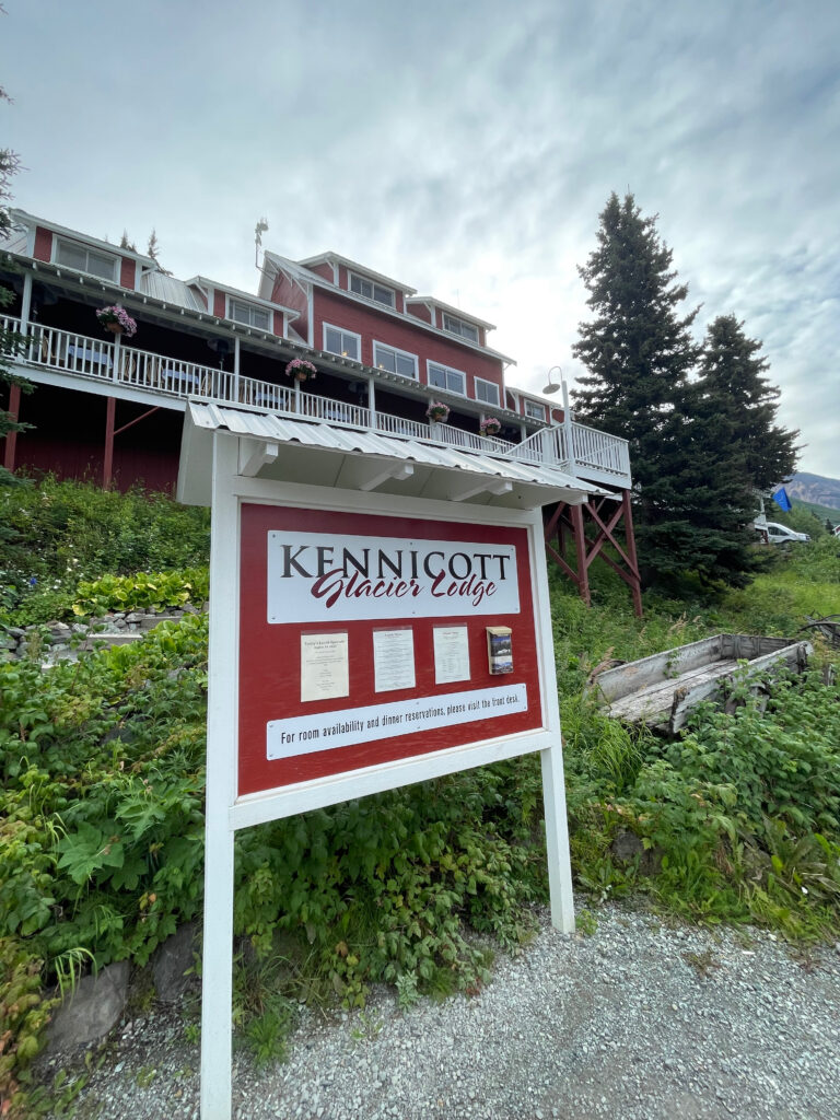 The Kennicott Glacier Lodge sign, along with the lodge itself in the background, with clouds over head.