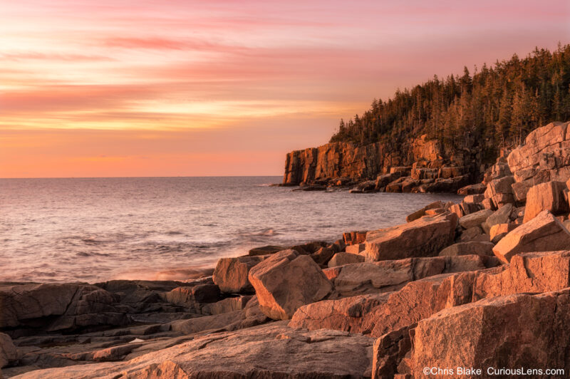 Sunrise at Acadia National Park with red glowing clouds, tall granite cliffs, and early morning light on the coastline.