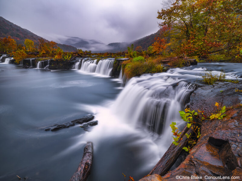 Sandstone Falls during a storm with dramatic sky, vibrant fall colors, and flowing water, captured minutes after sunset.