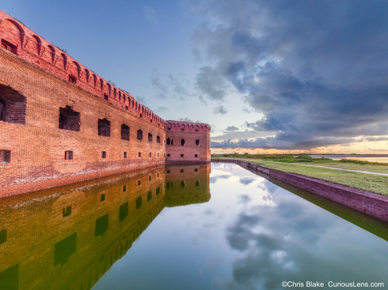 Fort Jefferson at sunrise in Dry Tortugas National Park with pre-sunrise clouds, still waters, and historical fort entrance.