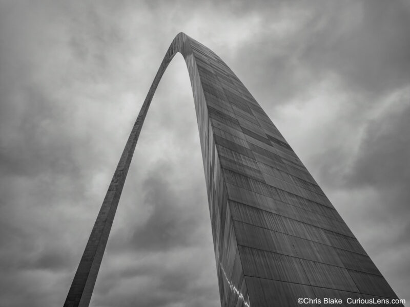 Gateway Arch in winter with dark sky, snow, ice-covered stainless-steel structure, and contrasting backdrop.