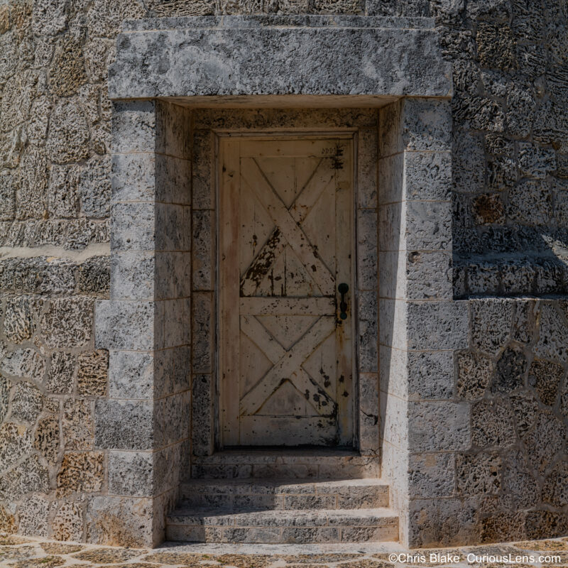 Detailed photograph of the Boca Chita Lighthouse on Boca Chita Key in Biscayne Bay National Park. The image emphasizes the texture of the coral bricks used in the lighthouse's construction, contrasting with the smooth grain of the wooden door. This iconic 1930s lighthouse, built by Mark Honeywell, offers views of nearby islands and the Miami skyline from its observation deck.