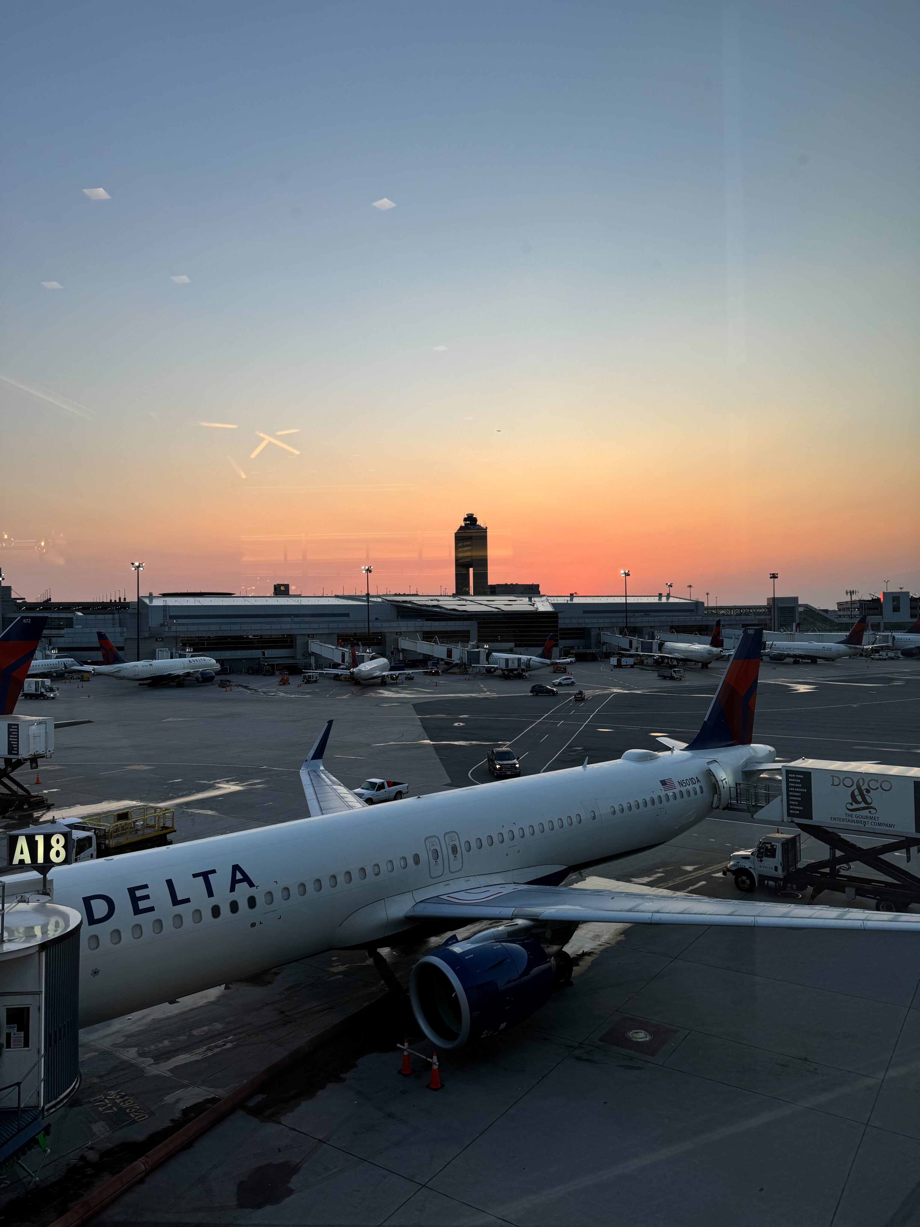 A Delta Airlines A321 neo parked at the gate at Logan Aiport. Taken at sunrise with a yellow and orange sky in the background. 