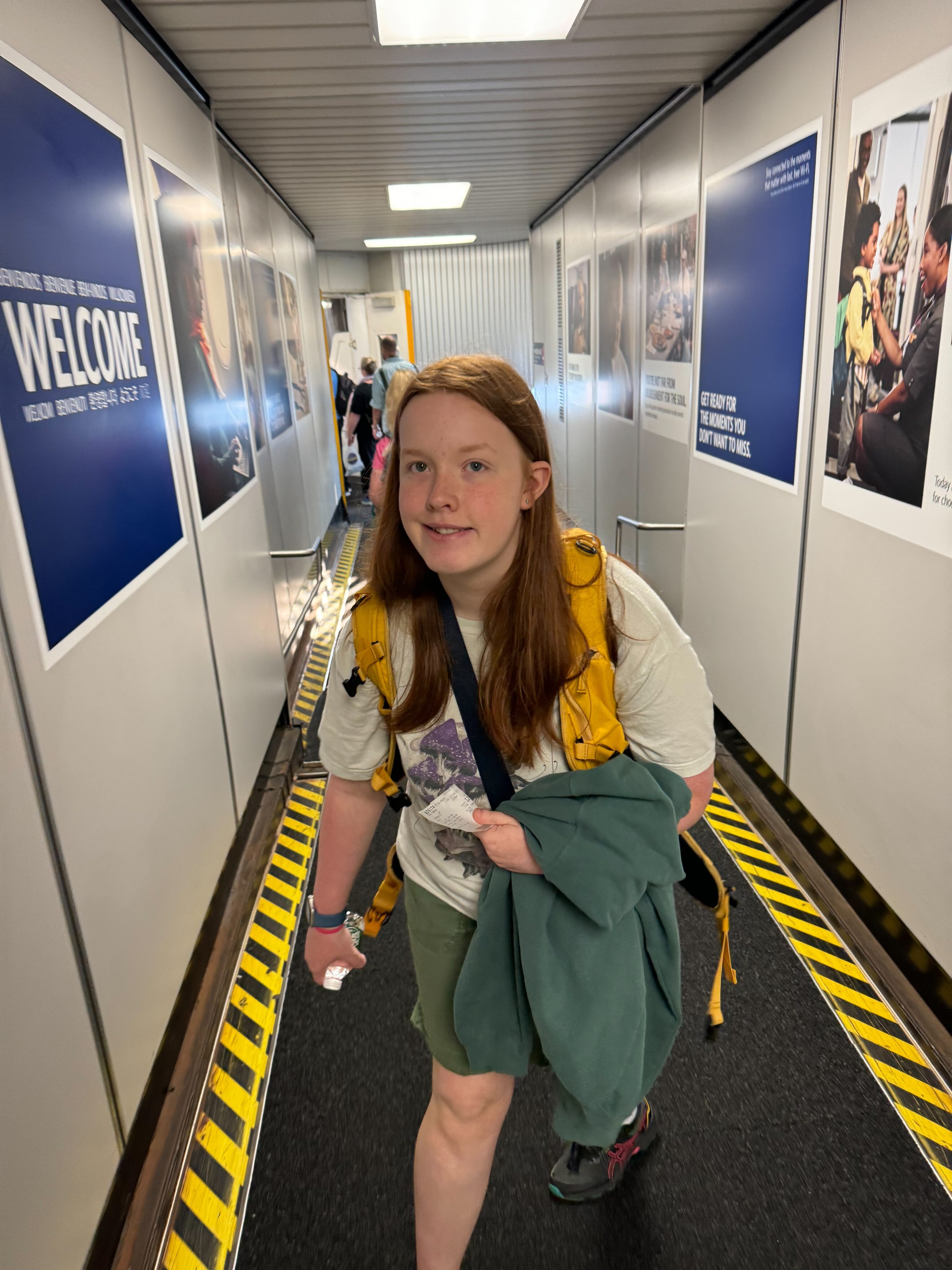 Cameron wearing her yellow camera backpack, walking backwards down the jet way getting onto the airplane.