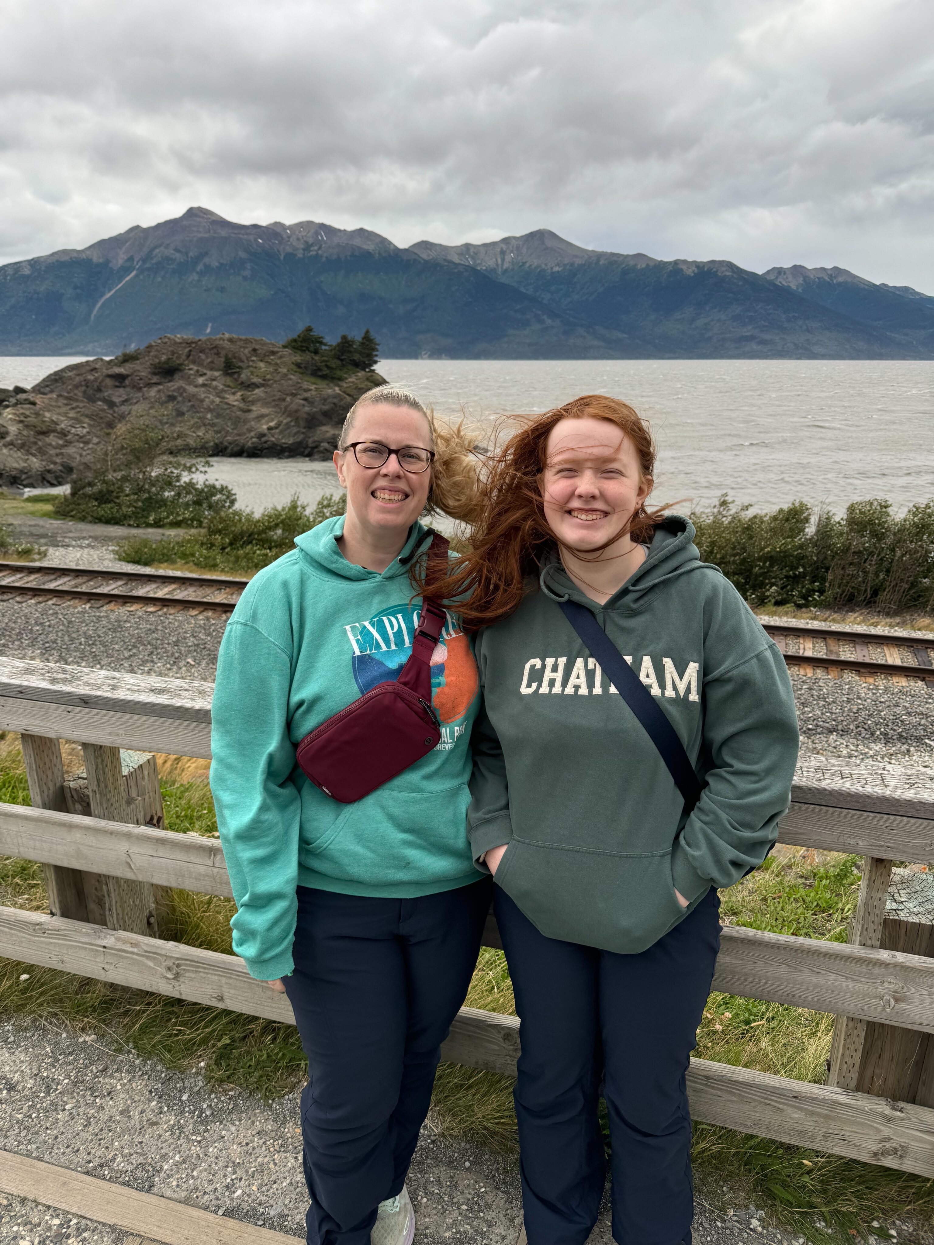 Cat and Cameron standing at one of the overlooks on rt1 in Alaska - the wind is blowing everyone's hair. The Turnagain Arm can be seen in the background.