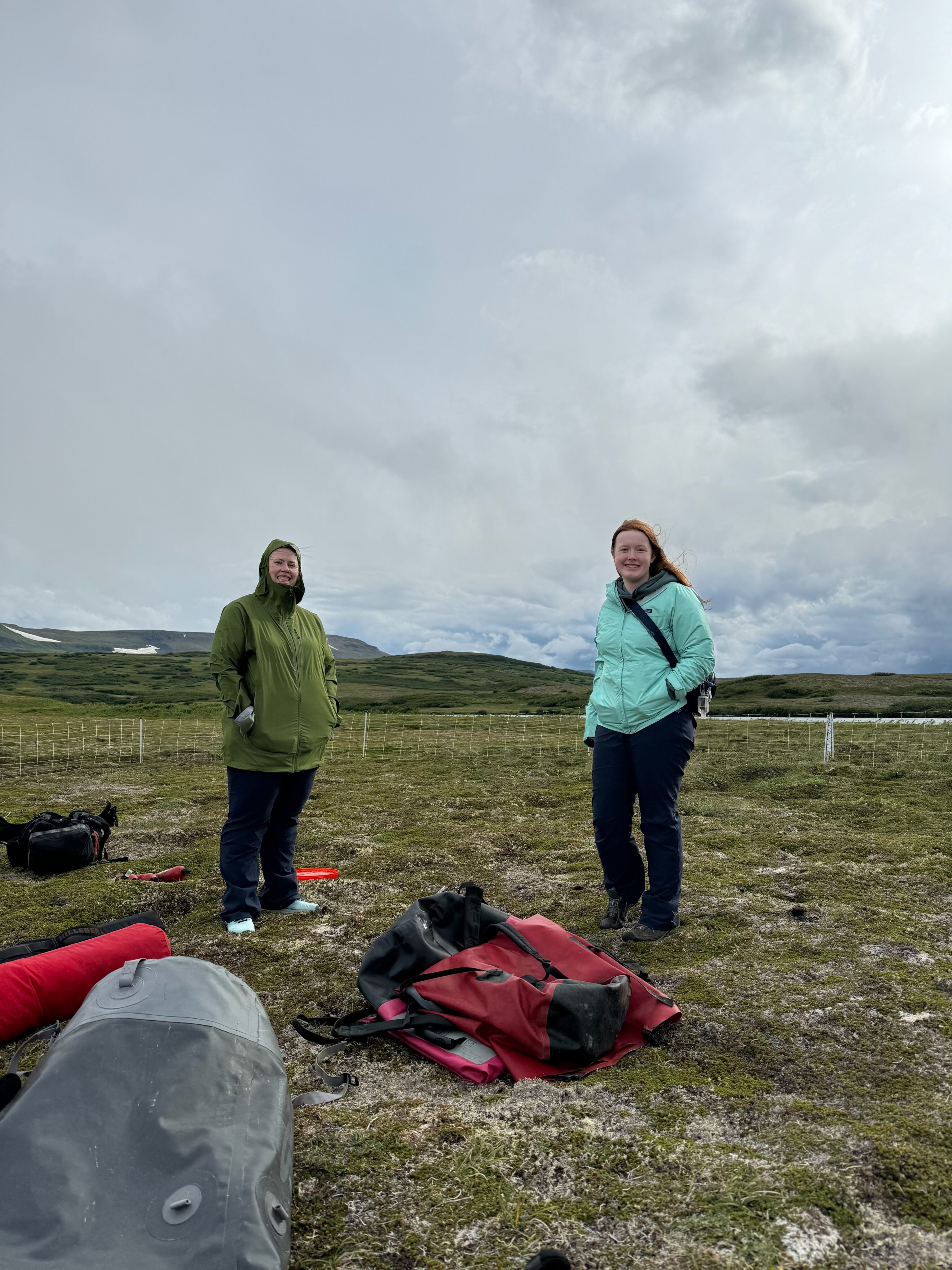 Cat and Cameron standing in winter clothing, on the tundra setting up camp near Crosswinds Lake - in Katmai National Park.