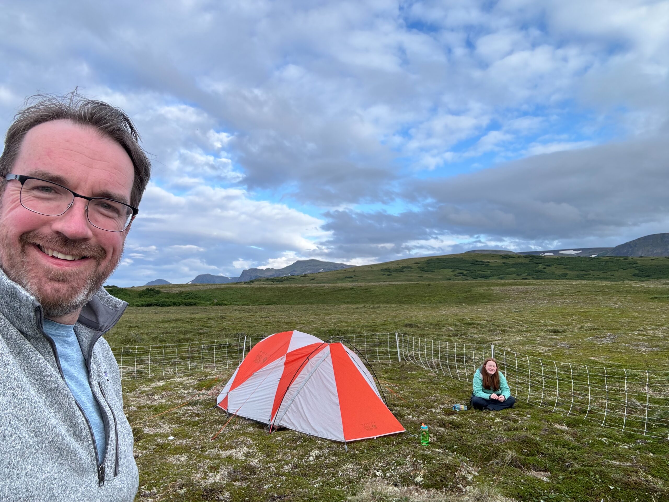 Cameron sitting by the electric fence and our tent, with Chris standing in the foreground inside our camp at Katmai National Park.