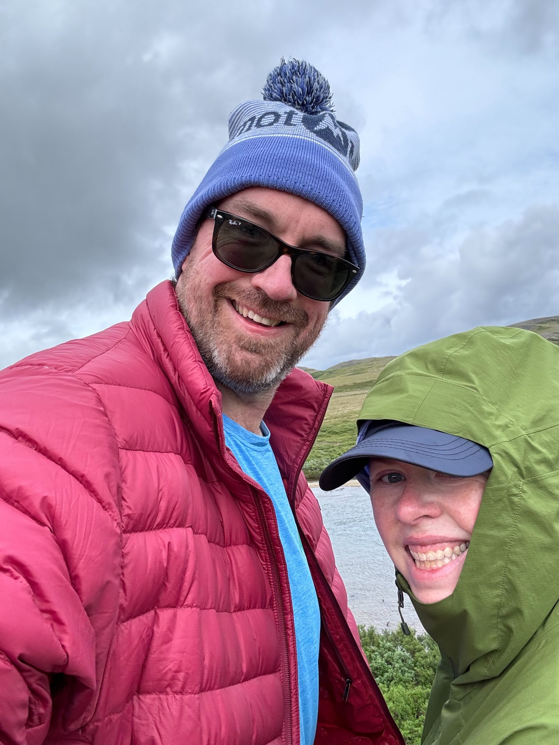 Cat wearing her rain gear and myself wearing a blue hat and red jacket pose for a photo on the river in Katmai National Park.