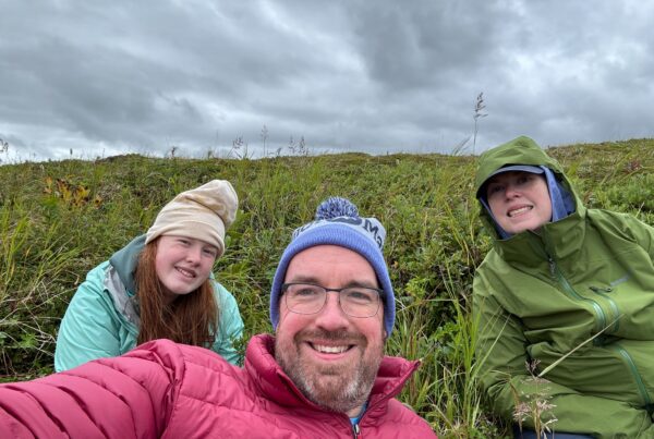 Cat, Cameron and myself all pose for a photo while sitting in the middle of the bank by the river. All of us wearing cold weather and rain gear.