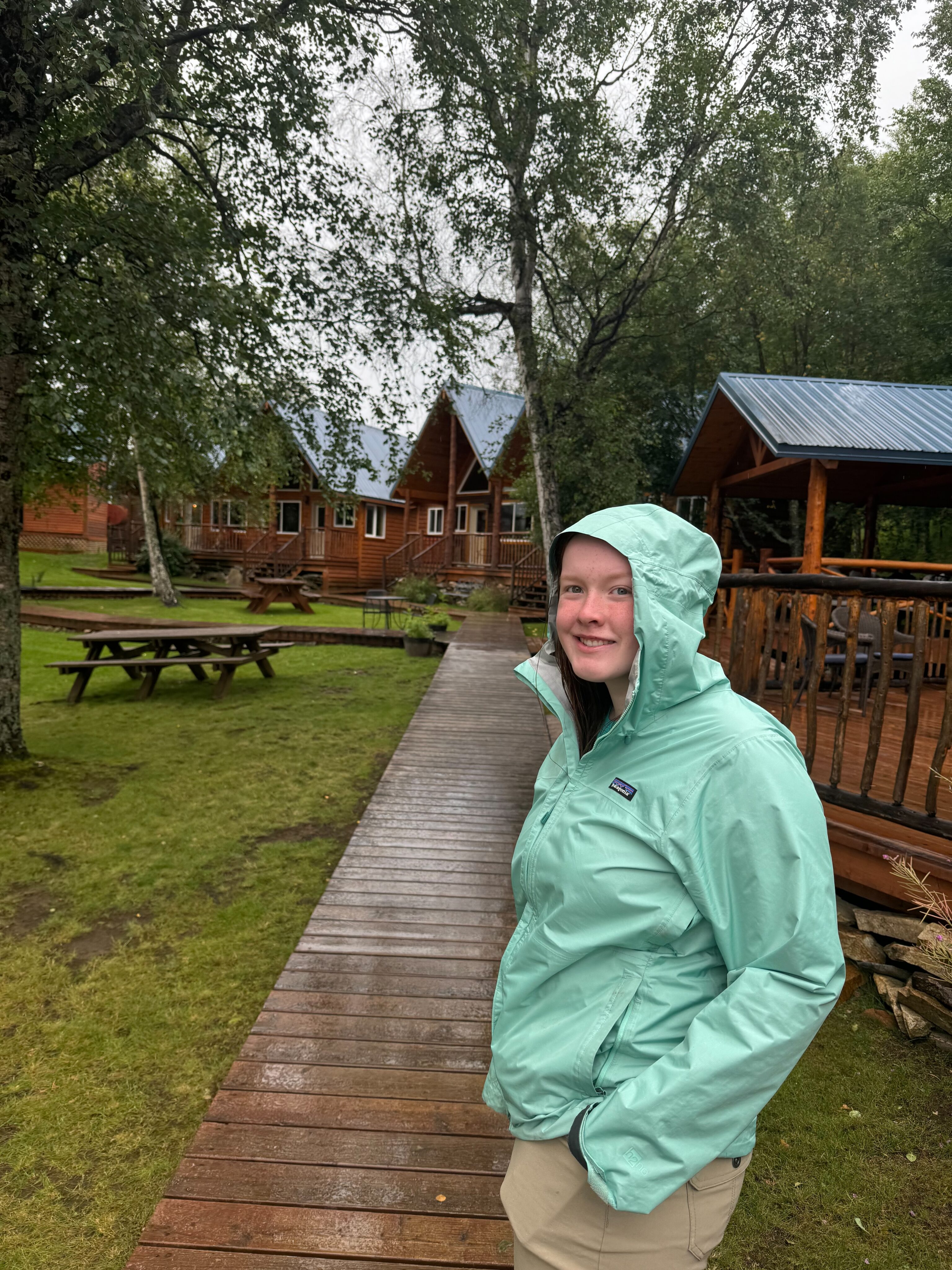 Cameron wearing her rain coat walking in the rain on the boardwalk at the Lake Clark Lodge in Port Alsworth.