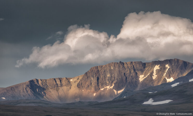 Dramatic mountain landscape with clouds in Katmai National Park, Alaska, capturing the interplay of light and shadow on rugged peaks.