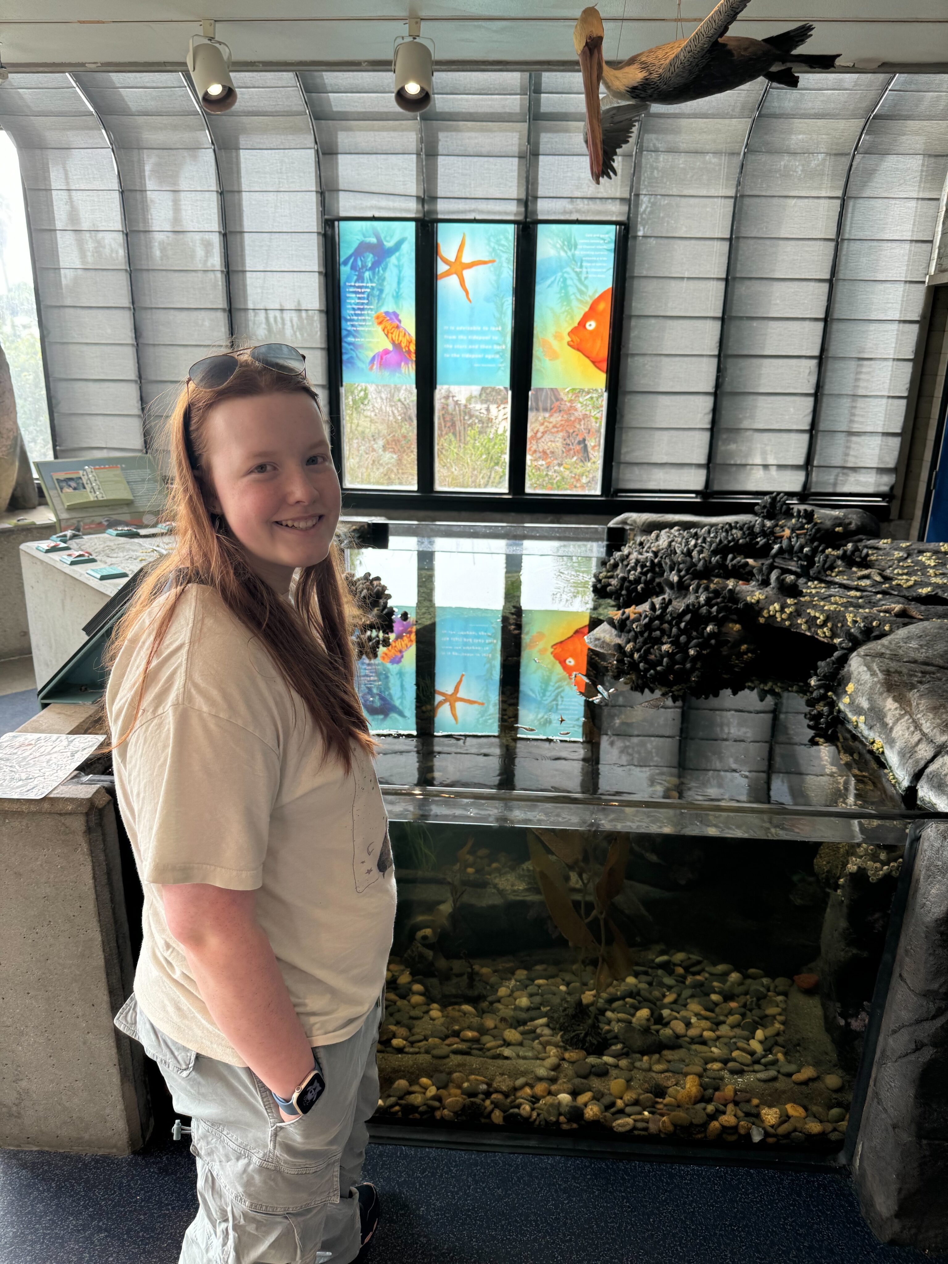 Cameron smiling with her hands in her pockets inside the Channel Island Visitors Center - in front of the fish tank.