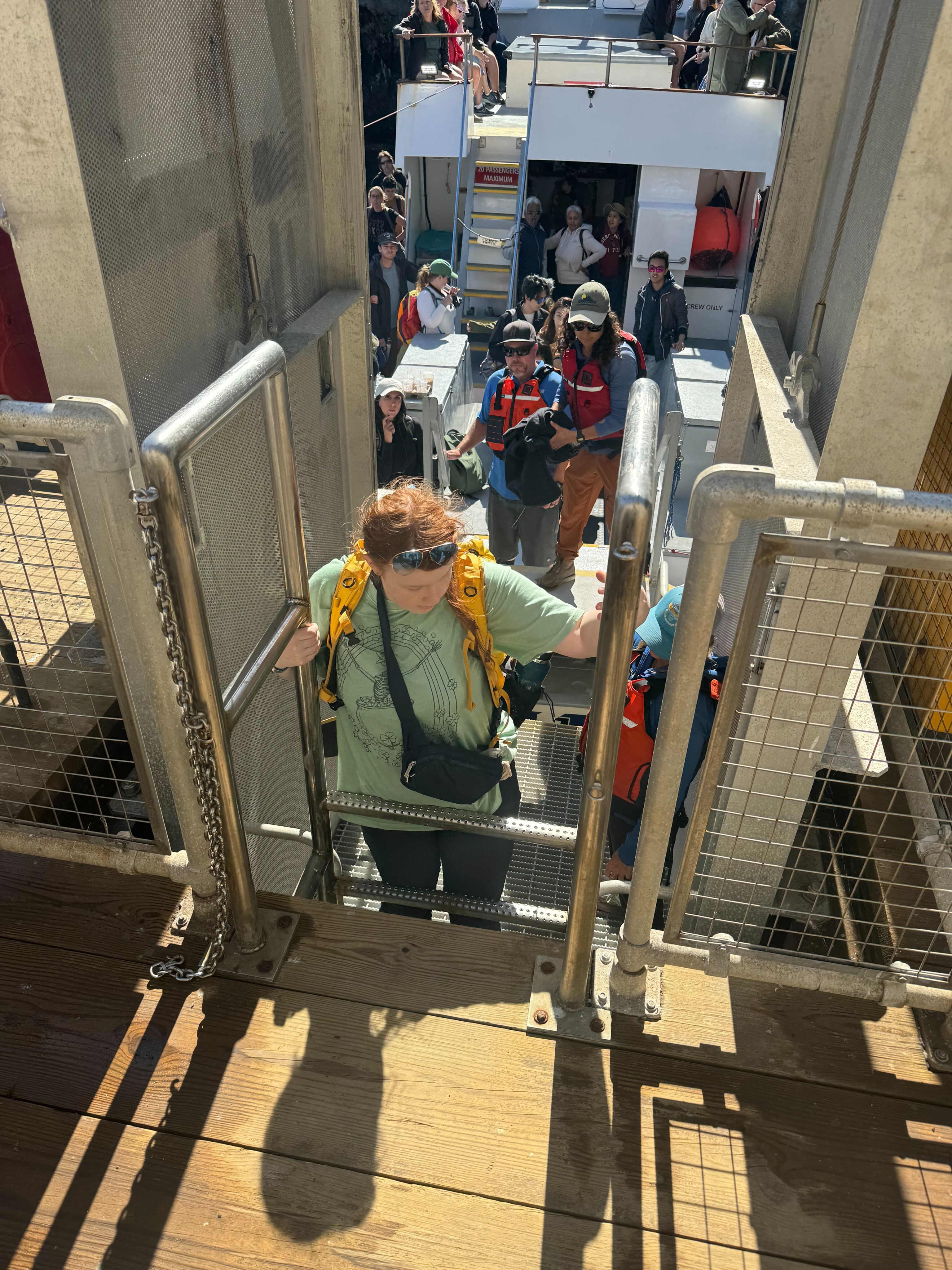 Cameron in a t-shirt and wearing her camera backpack climbing the ladder to the dock in Anacapa Island.