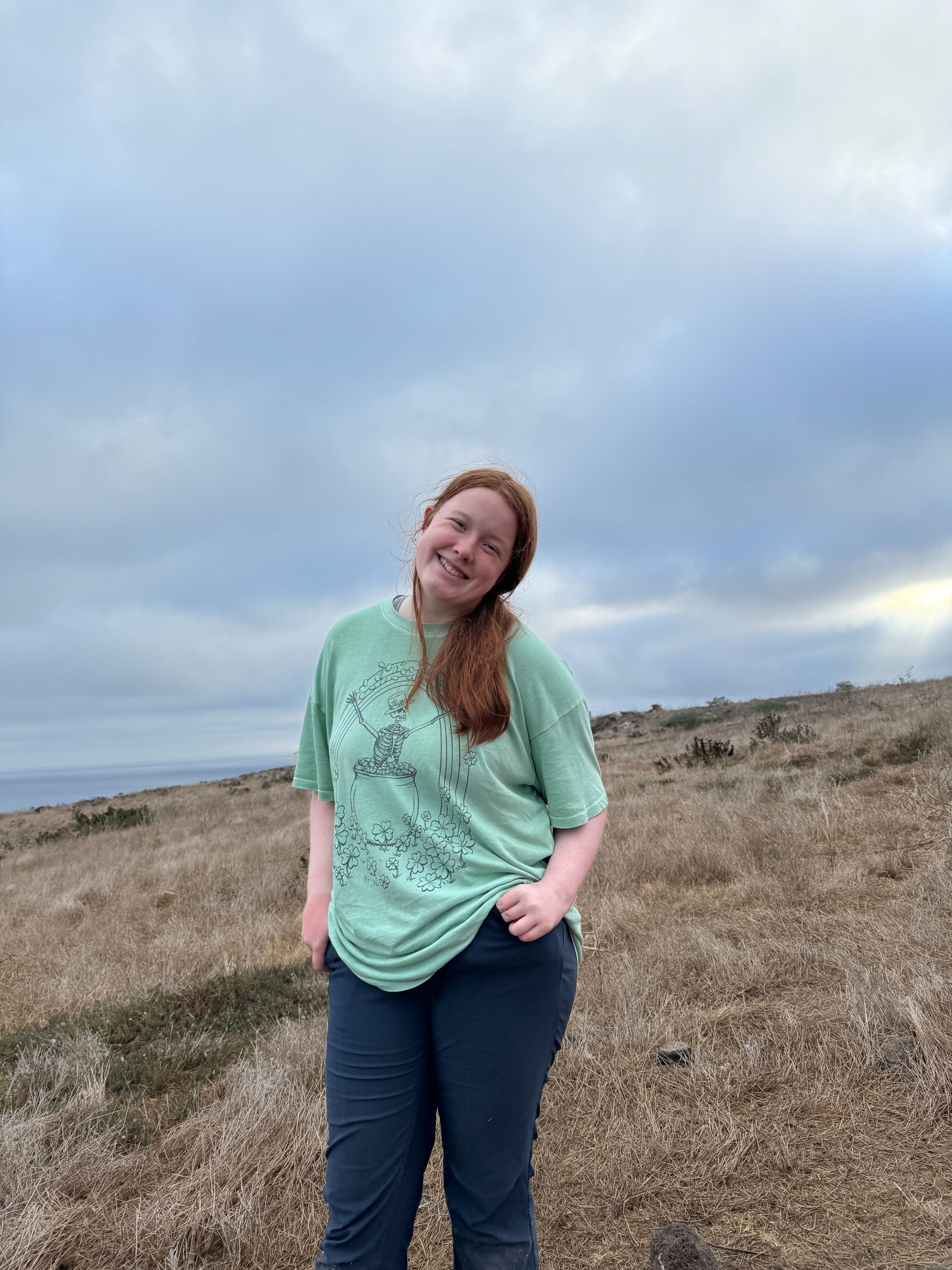 Cameron posing in a t-shirt and hiking pants on the open trail in the Channel Islands. A cloudy sky is overhead.