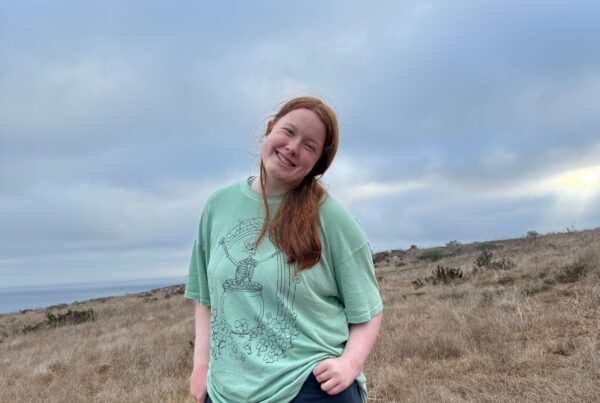 Cameron posing in a t-shirt and hiking pants on the open trail in the Channel Islands. A cloudy sky is overhead.