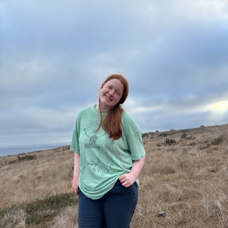 Cameron posing in a t-shirt and hiking pants on the open trail in the Channel Islands. A cloudy sky is overhead.