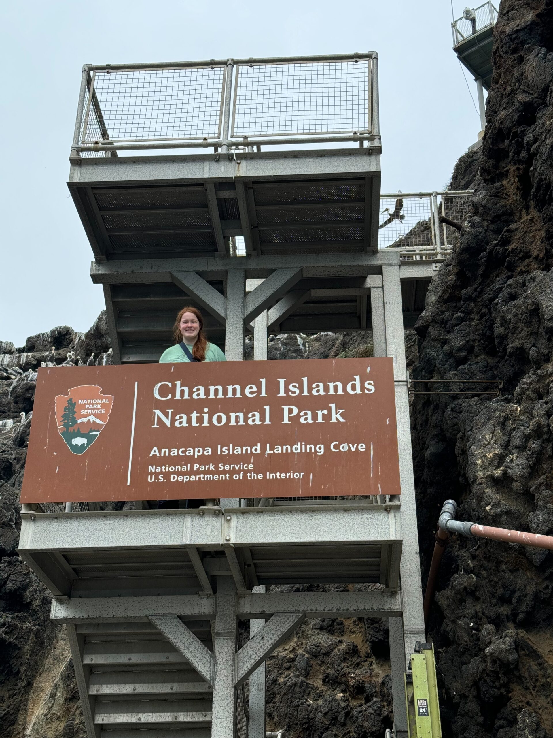 Cameron standing on one of the landings on the stairs leading up from the dock. The Channel Islands National Park sign is in front of her.