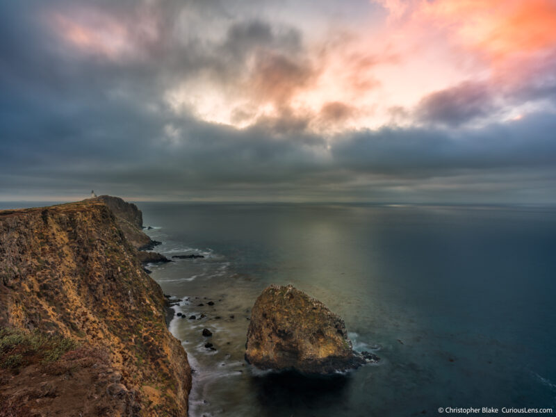 Sunrise at Anacapa Island in Channel Islands National Park, with cliffs, lighthouse, soft water, and breaking clouds after a storm.